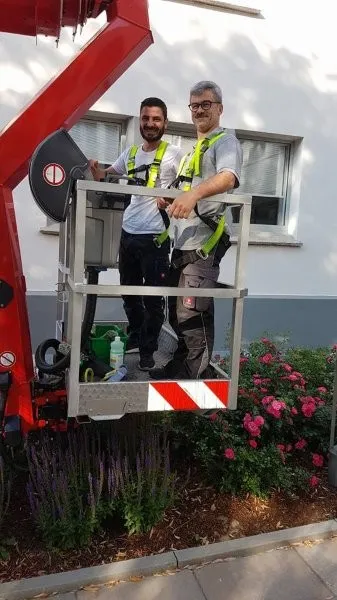 Zwei Mitarbeiter stehen in einer Hebebühne bereit für einen Gebäudereinigungs-Einsatz